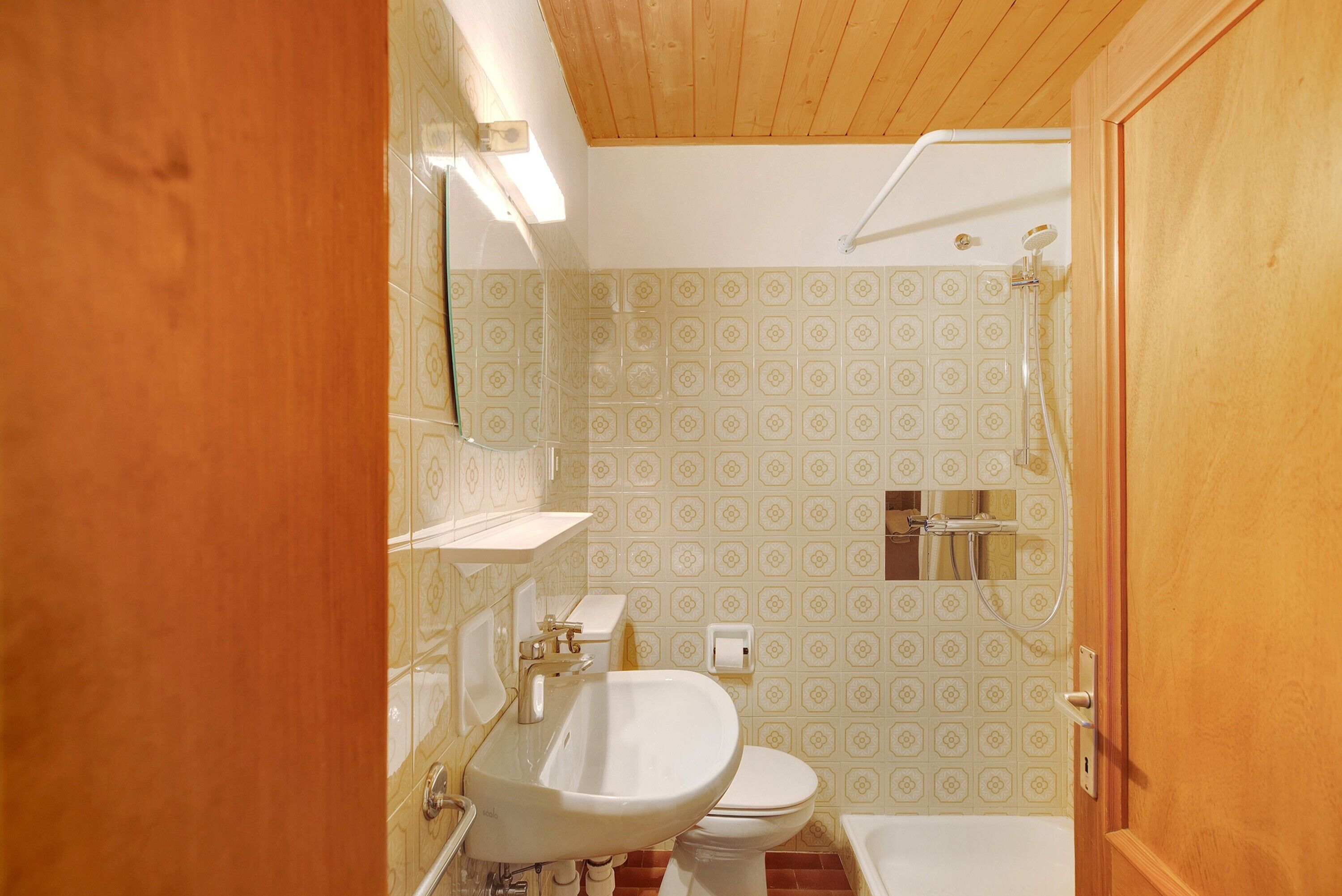 Ein Badezimmer mit Toilette, Waschbecken, Dusche und gemusterten Fliesen.