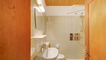 Ein Badezimmer mit Toilette, Waschbecken, Dusche und gemusterten Fliesen.