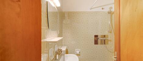 Une salle de bain équipée de toilettes, d’un lavabo, d’une douche et de carreaux décoratifs.