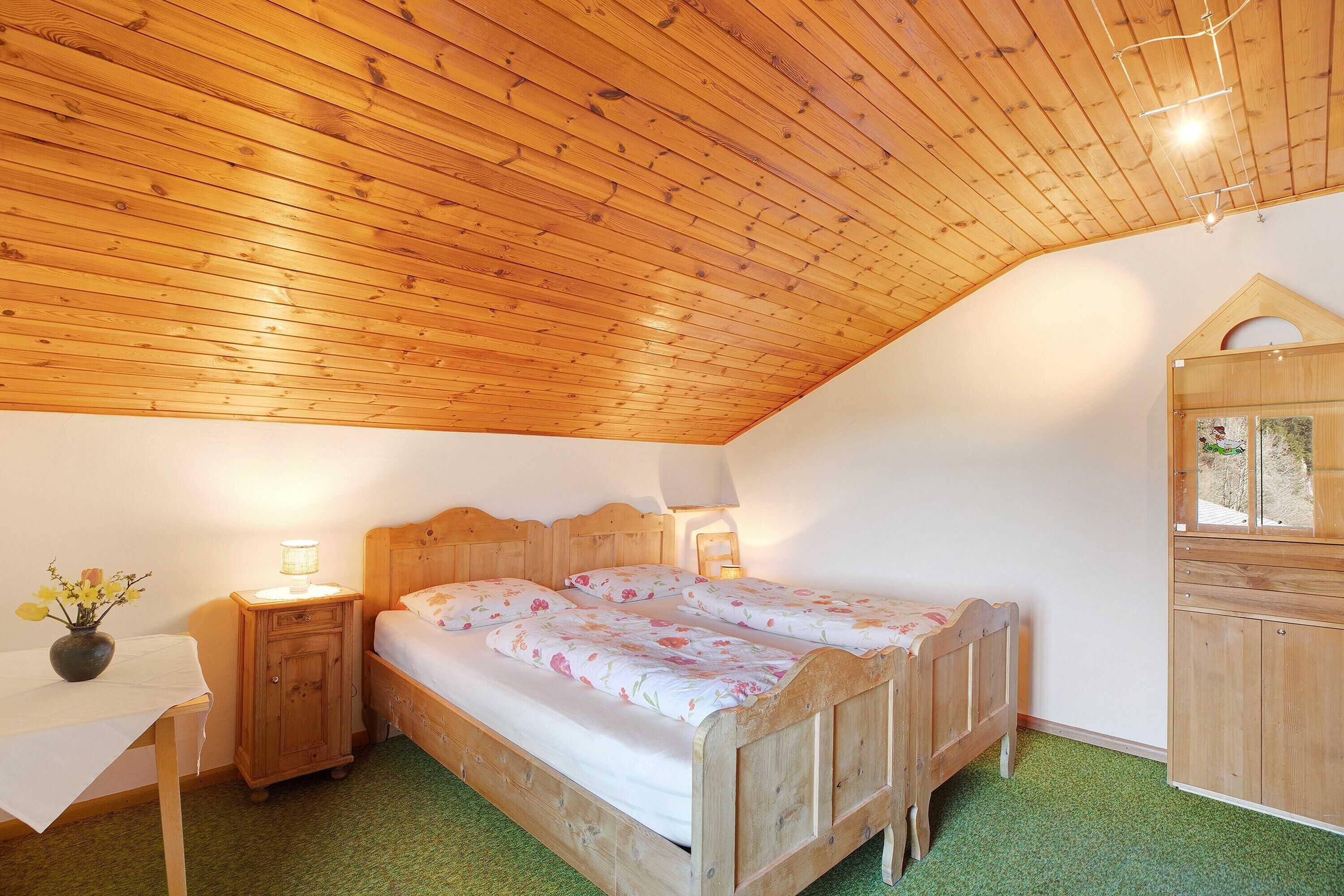Ein Schlafzimmer mit Holzbalkendecke, einem Bett mit Blumenmuster-Bettwäsche, einem Nachttisch mit Lampe und einem kleinen Schrank.