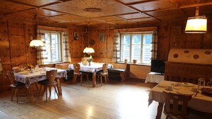 A wooden cabin with a dining area featuring tables and chairs, a fireplace, and large windows. - Holiday Apartment "Pischlhof Apt Lärche" with Mountain View, Balcony & Shared Garden (Aldino)
