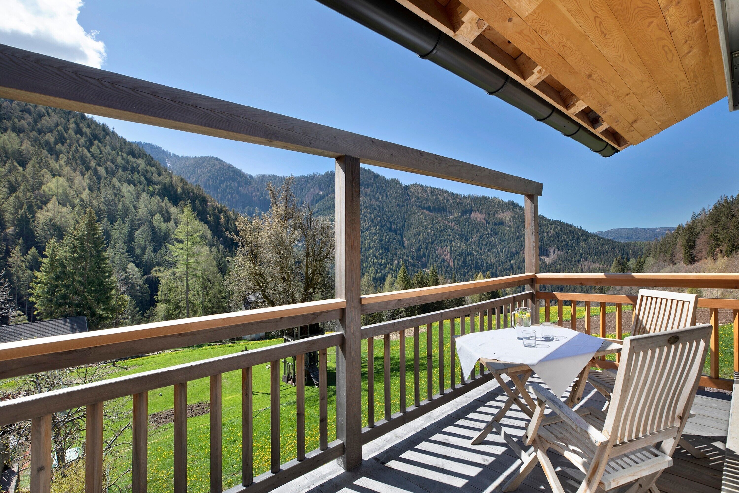 A wooden deck with a table and chairs, overlooking a mountainous landscape.