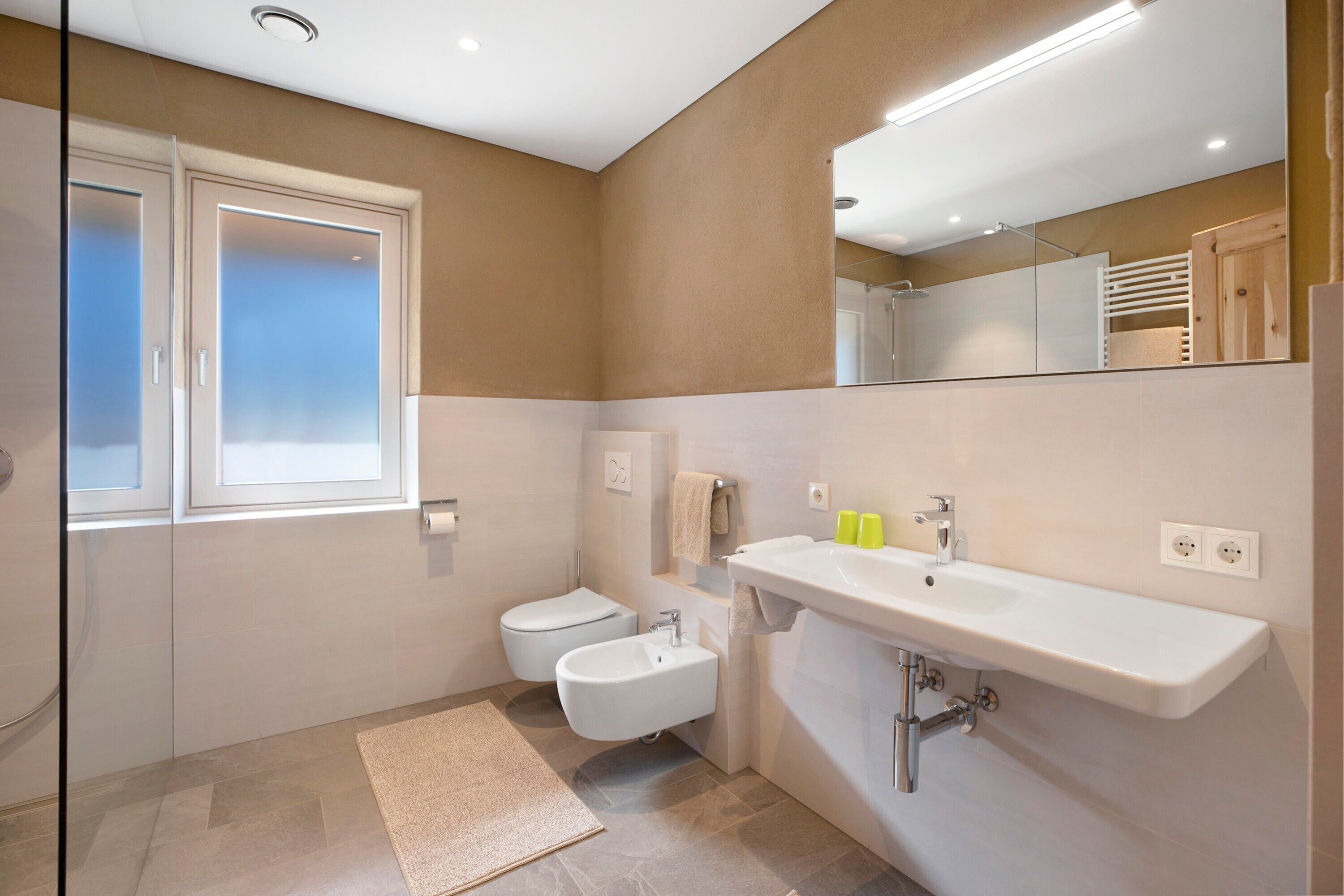 Une salle de bain moderne équipée de toilettes, d’un bidet, d’un lavabo et d’un miroir.