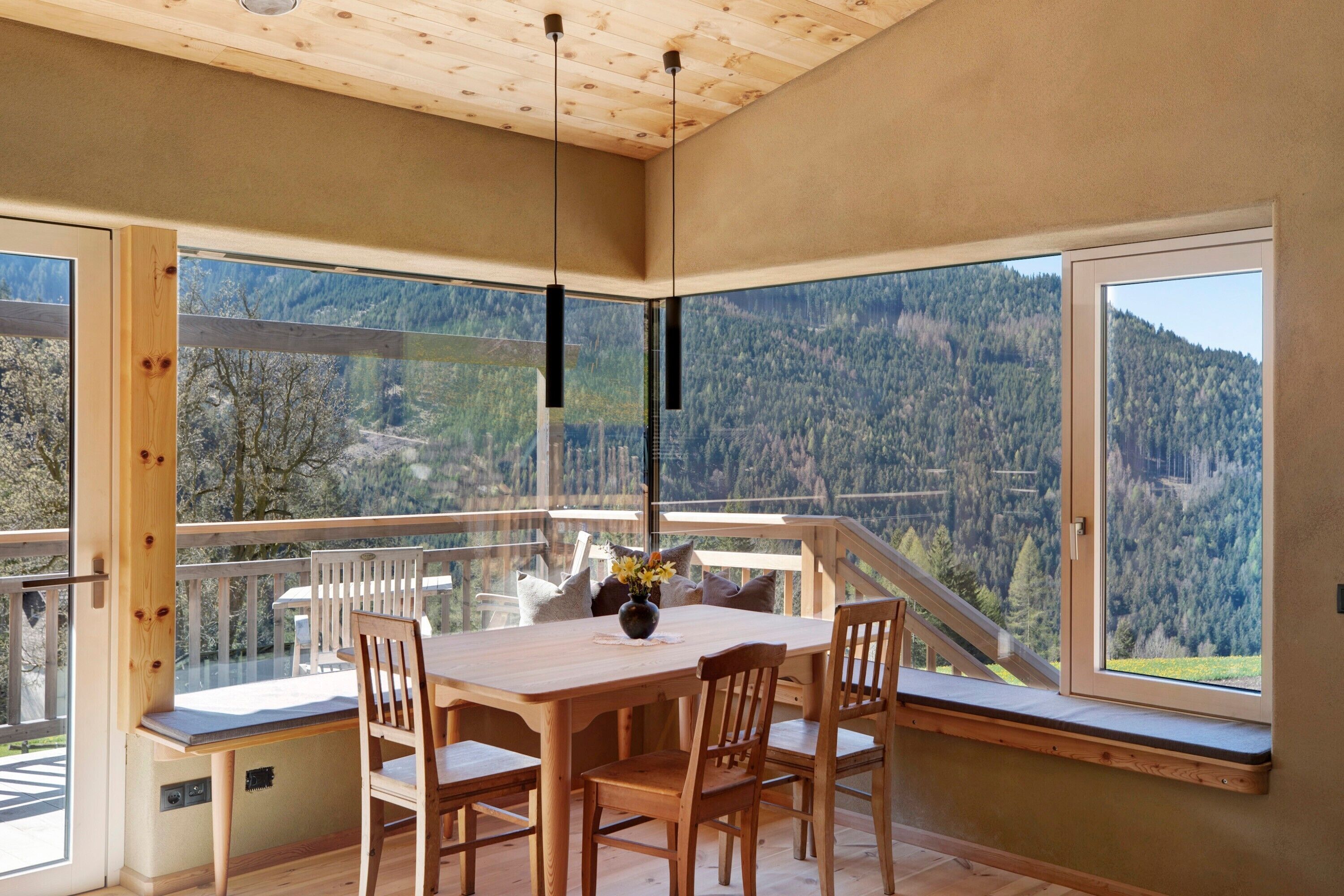 Ein Essbereich mit Tisch und Stühlen, große Fenster mit Blick auf die Berge und einer Holzbalkendecke.