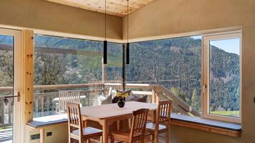 Ein Essbereich mit Tisch und Stühlen, große Fenster mit Blick auf die Berge und einer Holzbalkendecke.