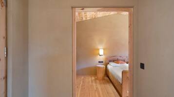 Un corridoio stretto che porta a una camera da letto con pavimento in legno, un letto con cuscini, un comodino e una lampada a muro.