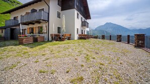 Un edificio de dos pisos con balcón, asientos exteriores y vistas a las montañas.