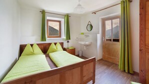 Una habitación con cama de madera, ventana con cortinas, mesita de noche con lámpara, espejo y puerta que da al exterior.