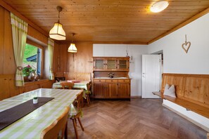 A wooden interior with a dining table, chairs, a bench, a cabinet, and a hanging heart decoration.