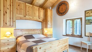 A wooden bedroom with a bed, nightstands, a chair, a window with curtains, and a wall-mounted decorative item. - Chalet 'Baita Bocheto' with Balcony & Terrace (Levico Terme)