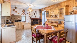 A rustic kitchen with wooden cabinets, a fireplace, a dining table with chairs, and a refrigerator. - Chalet 'Baita Bocheto' with Balcony & Terrace (Levico Terme)