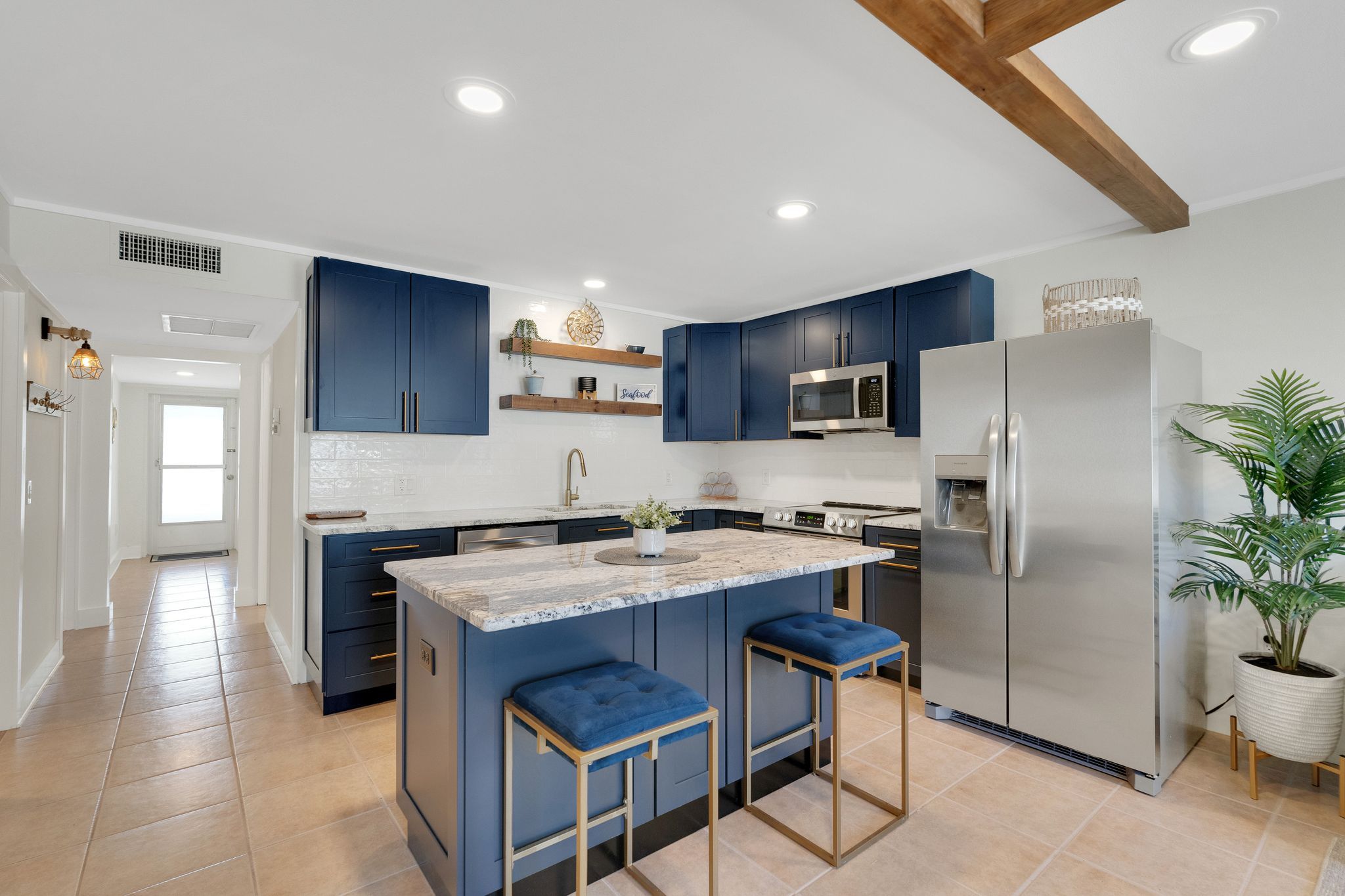 A modern kitchen with blue cabinets, a stainless steel refrigerator, and a marble island with bar stools.