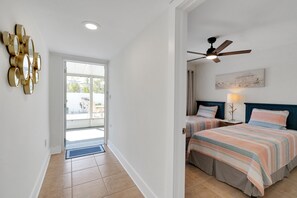 A bedroom with two beds, a ceiling fan, and a door leading to a balcony. - Blue Isle Oasis: Adorable, updated 2 bedroom cottage (Holmes Beach)