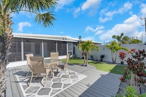 A modern outdoor patio with a round table and chairs, surrounded by a wooden deck and a glass enclosure.