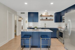 A modern kitchen with blue cabinets, a stainless steel refrigerator, and a central island with bar stools.