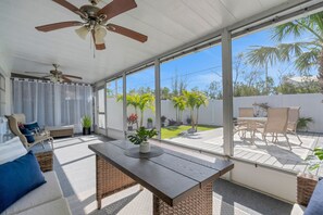 A covered patio area with a ceiling fan, wicker furniture, and a view of a landscaped backyard. - Blue Isle Oasis: Adorable, updated 2 bedroom cottage (Holmes Beach)