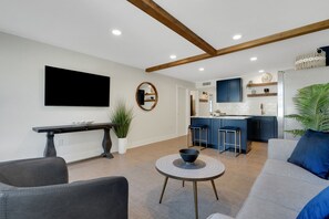 A modern living room with a flat-screen TV, a round mirror, a dining table, and a sofa. - Blue Isle Oasis: Adorable, updated 2 bedroom cottage (Holmes Beach)