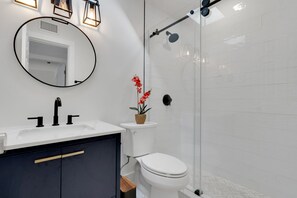 A modern bathroom with a round mirror, a sink, a toilet, and a shower area. - Blue Isle Oasis: Adorable, updated 2 bedroom cottage (Holmes Beach)