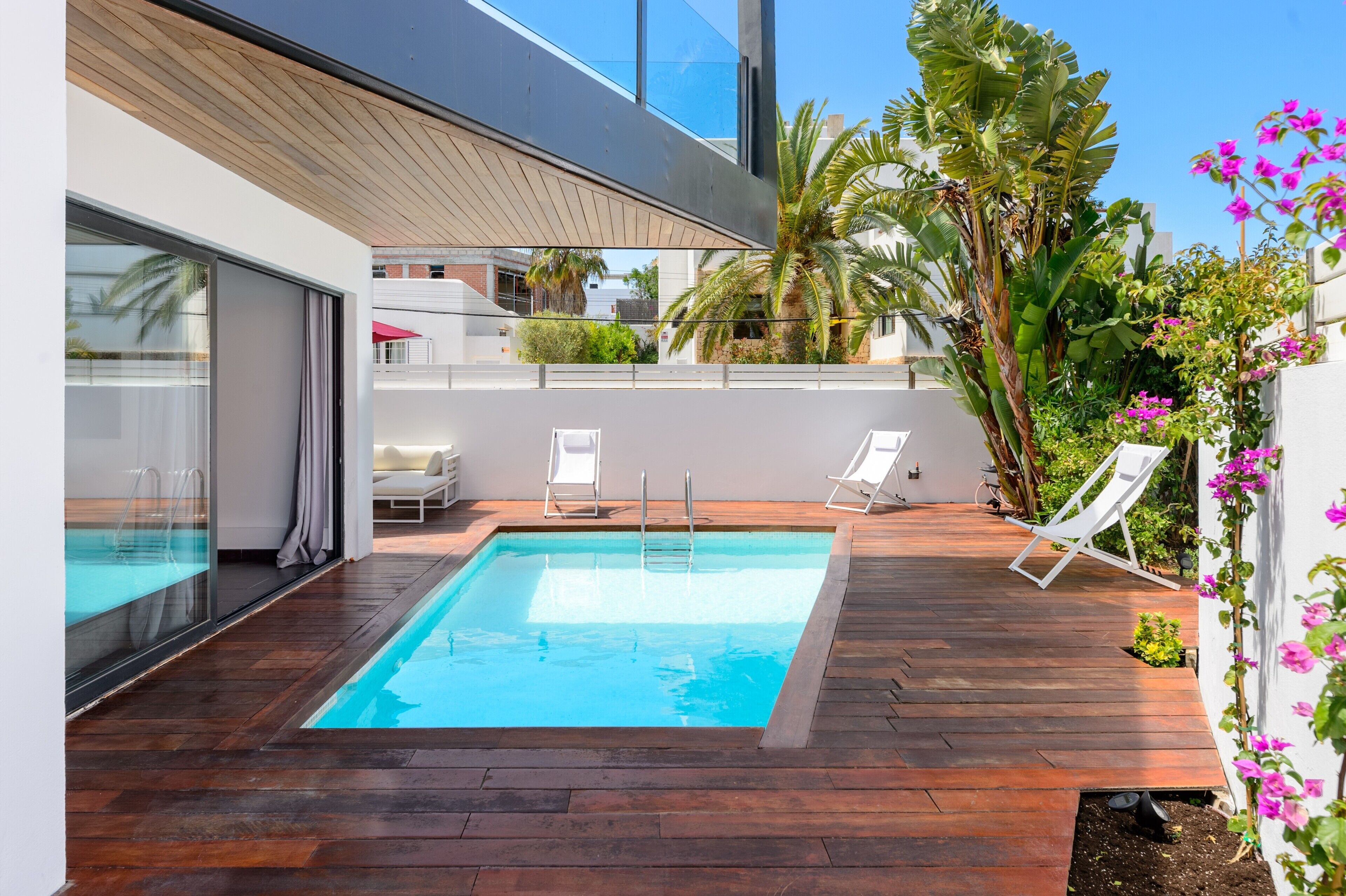 Ein moderner Poolbereich im Freien mit Holzterrasse, zwei Liegestühlen und einem Pool mit Glasverkleidung.
