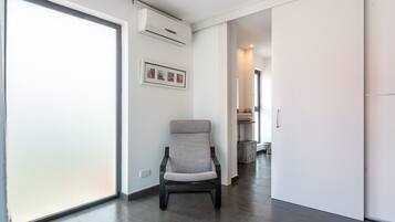 A modern interior with a sliding glass door, a grey upholstered chair, a framed picture on the wall, and a hallway leading to another room.
