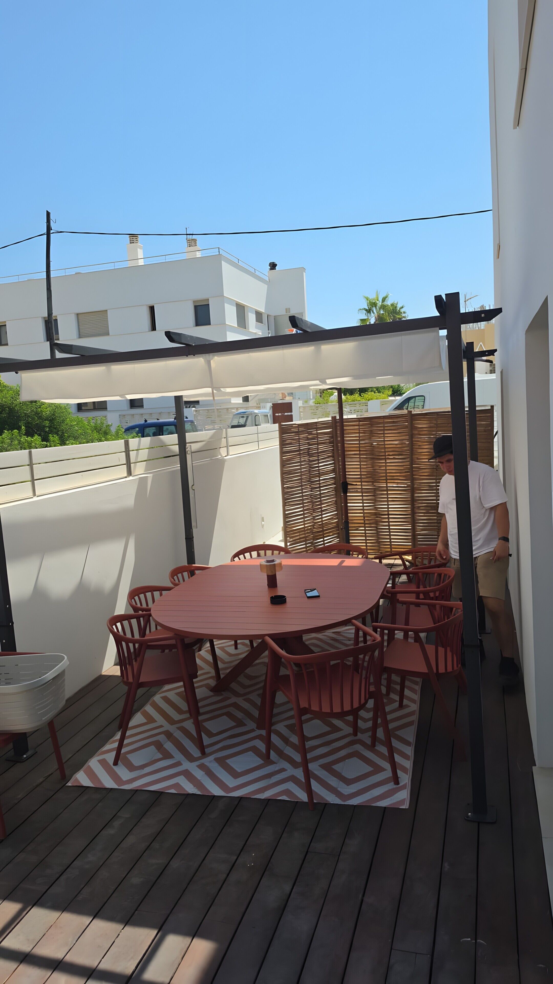 An outdoor patio with a round table and chairs, a basket, and a patterned rug.