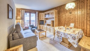 A cozy living room with a sofa, a dining table set for two, and wooden paneling on the walls.