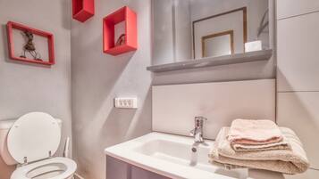 Une salle de bain avec des toilettes, un lavabo et un miroir. Il y a des boîtes de rangement rouges accrochées au mur.