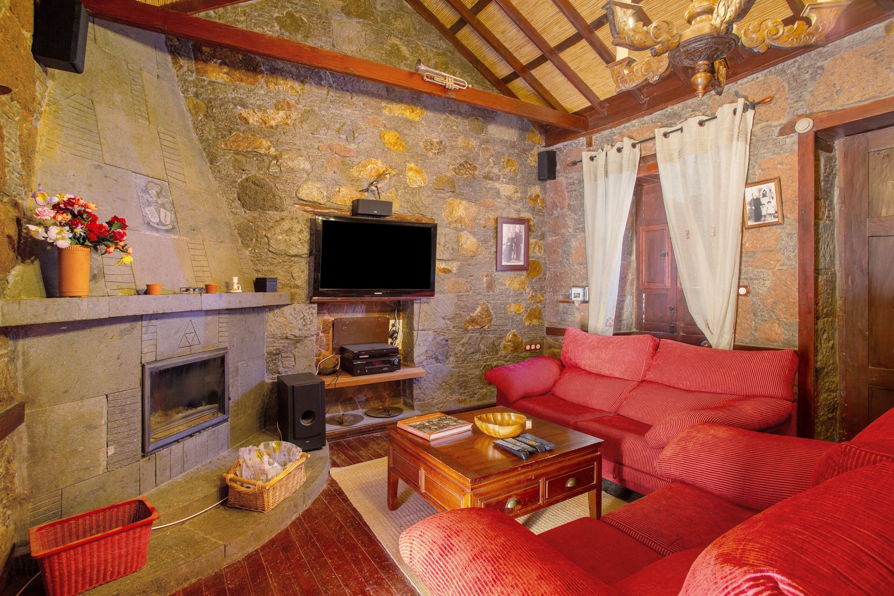 A cozy living room with a stone wall, a fireplace, a red sofa, and a television.