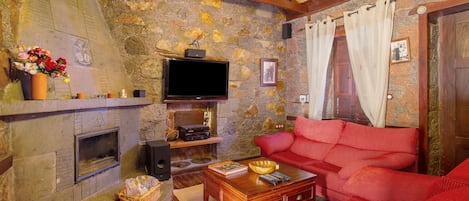 A cozy living room with a stone wall, a fireplace, a red sofa, and a television.