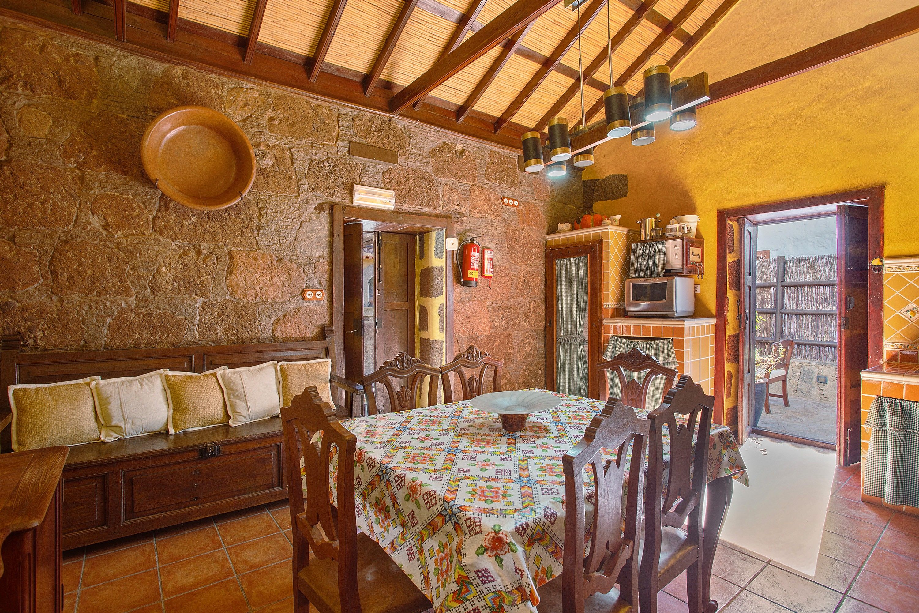 A dining area with a wooden table and chairs, a stone wall, and a ceiling with wooden beams.