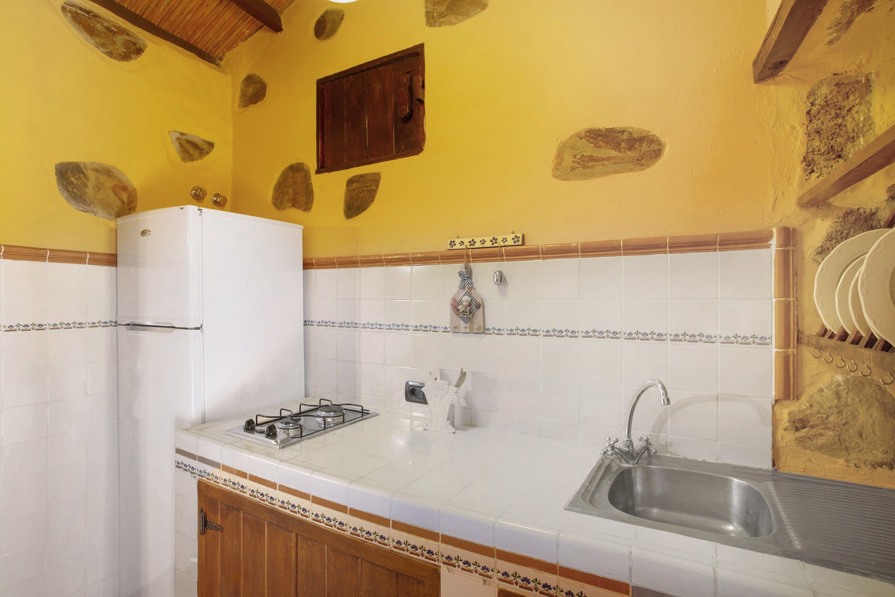 Una cocina con baldosas blancas, un refrigerador blanco, una estufa a gas, un lavamanos y azulejos decorativos.