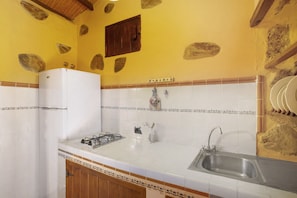 Una cocina con baldosas blancas, un refrigerador blanco, una estufa a gas, un lavamanos y azulejos decorativos.