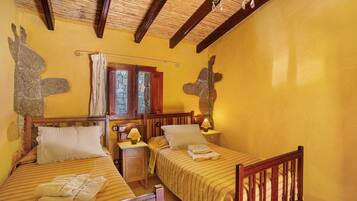 A room with two beds, wooden headboards, a nightstand with a lamp, and a stone wall.