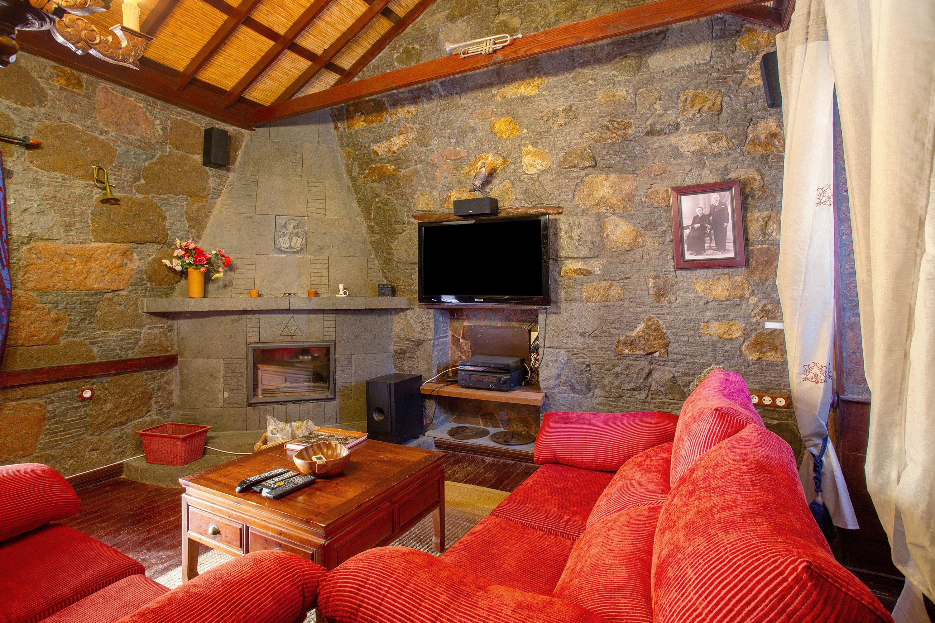 A cozy living room with a stone fireplace, a flat-screen TV mounted above it, and a comfortable red sofa.