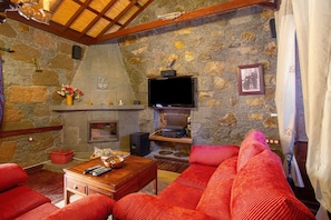 A cozy living room with a stone fireplace, a flat-screen TV mounted above it, and a comfortable red sofa. - Country House 'Bentayga Sensation' with Private Pool (Tejeda)