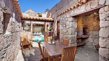Un espacio al aire libre con paredes de piedra, una mesa y sillas de madera, una piscina y una chimenea de piedra.