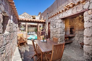 A stone-walled outdoor area with a wooden table and chairs, a pool, and a stone fireplace. - Country House 'Bentayga Sensation' with Private Pool (Tejeda)