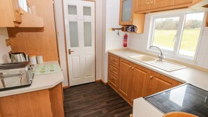 Cocina compacta con armarios de madera, encimera blanca, un lavamanos y ventana con vistas a una zona verde.