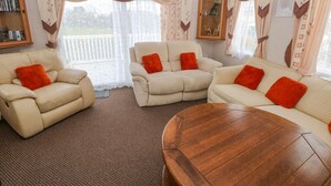 Una sala de estar acogedora con una mesa de centro de madera, dos sofás color beige con cojines naranjas y una estantería.