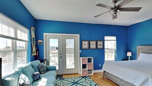 Ein Schlafzimmer mit einem Bett, Deckenventilator, Fenster, Tür, Sofa und einem gemusterten Teppich.