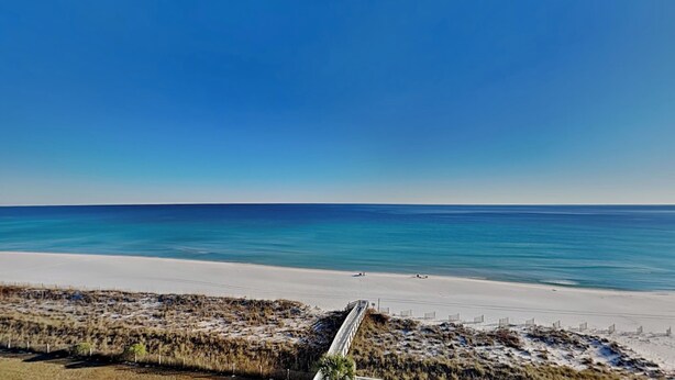 A beach with a clear sky, a sandy shore, and a white fence in the foreground. - Regency Towers #801 West | Beachfront, Pool! (Pensacola Beach)