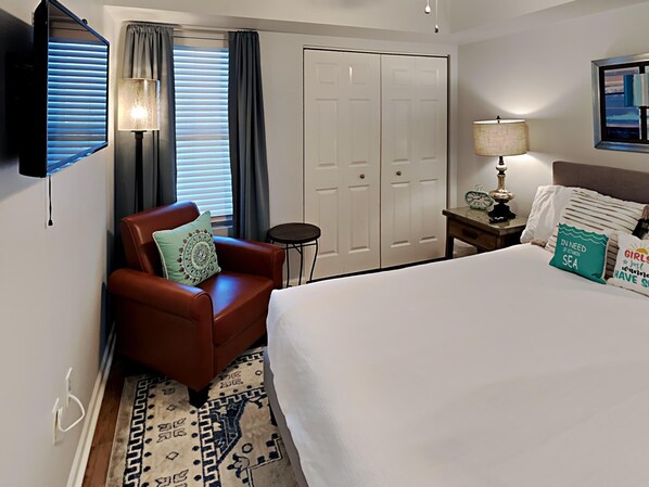 A hotel room with a bed, a chair, a desk, a lamp, a clock, and a wardrobe. - Terrace at Pelican Beach #703 | Gulf View + Resort Amenities (Destin)