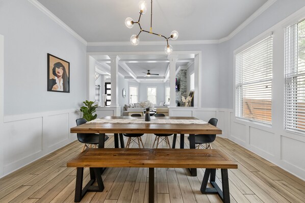 A dining area with a wooden table and benches, white walls, and a modern chandelier.