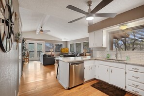 A modern kitchen with white cabinets, a stainless steel dishwasher, and a ceiling fan.