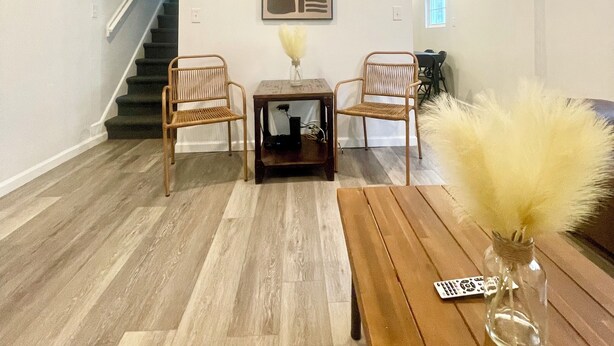 Un vaste espace de vie comprenant une table basse en bois, deux fauteuils en osier, une petite table d’appoint avec un vase, et un escalier menant à une autre pièce.