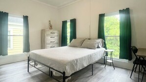 Une chambre à coucher avec un lit, une commode, une chaise et une fenêtre avec des rideaux.
