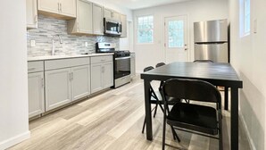 Une cuisine moderne avec un revêtement de sol en bois clair, des armoires blanches, des appareils électroménagers en acier inoxydable et un coin repas comprenant une table et des chaises.