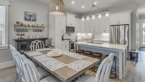 A modern kitchen with white cabinets, a central island, and a dining area with a wooden table and chairs.