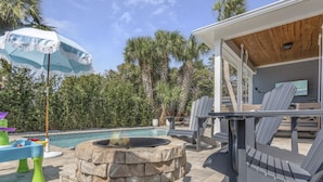 A poolside area with a stone fire pit, lounge chairs, and a covered seating area.
