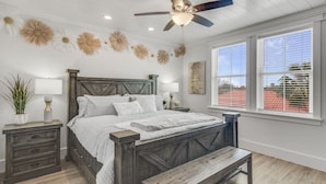 A bedroom with a wooden bed, white walls, a ceiling fan, and a large window with blinds.